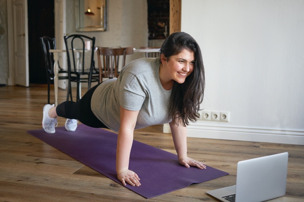 Woman on an exercise mat performing a plank exercise in front of her computer