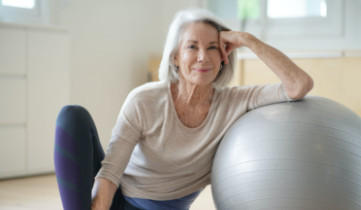 Image of a older lady sitting next to a yoga ball ready to exercise