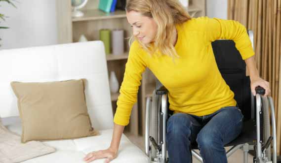 A woman in a yellow shirt transfers from a wheelchair into a bed