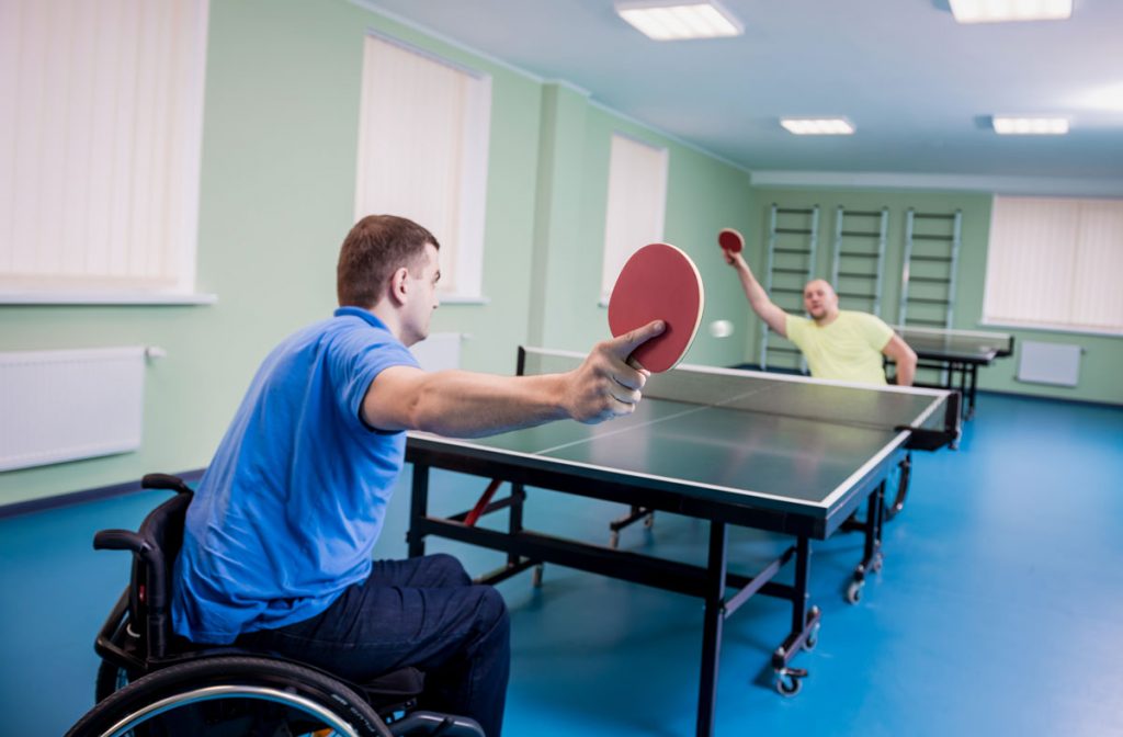 Two men with disability in wheelchairs playing table tennis against each other