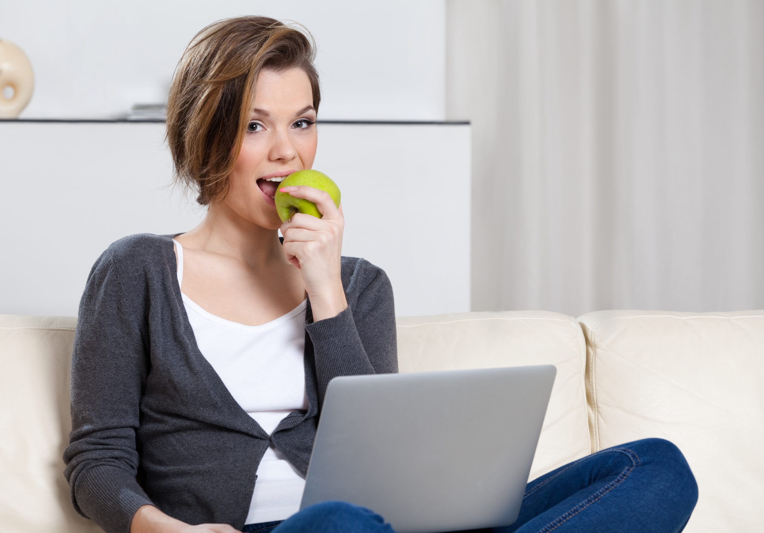 Young woman sitting on a couch eating an apple to support good mental health