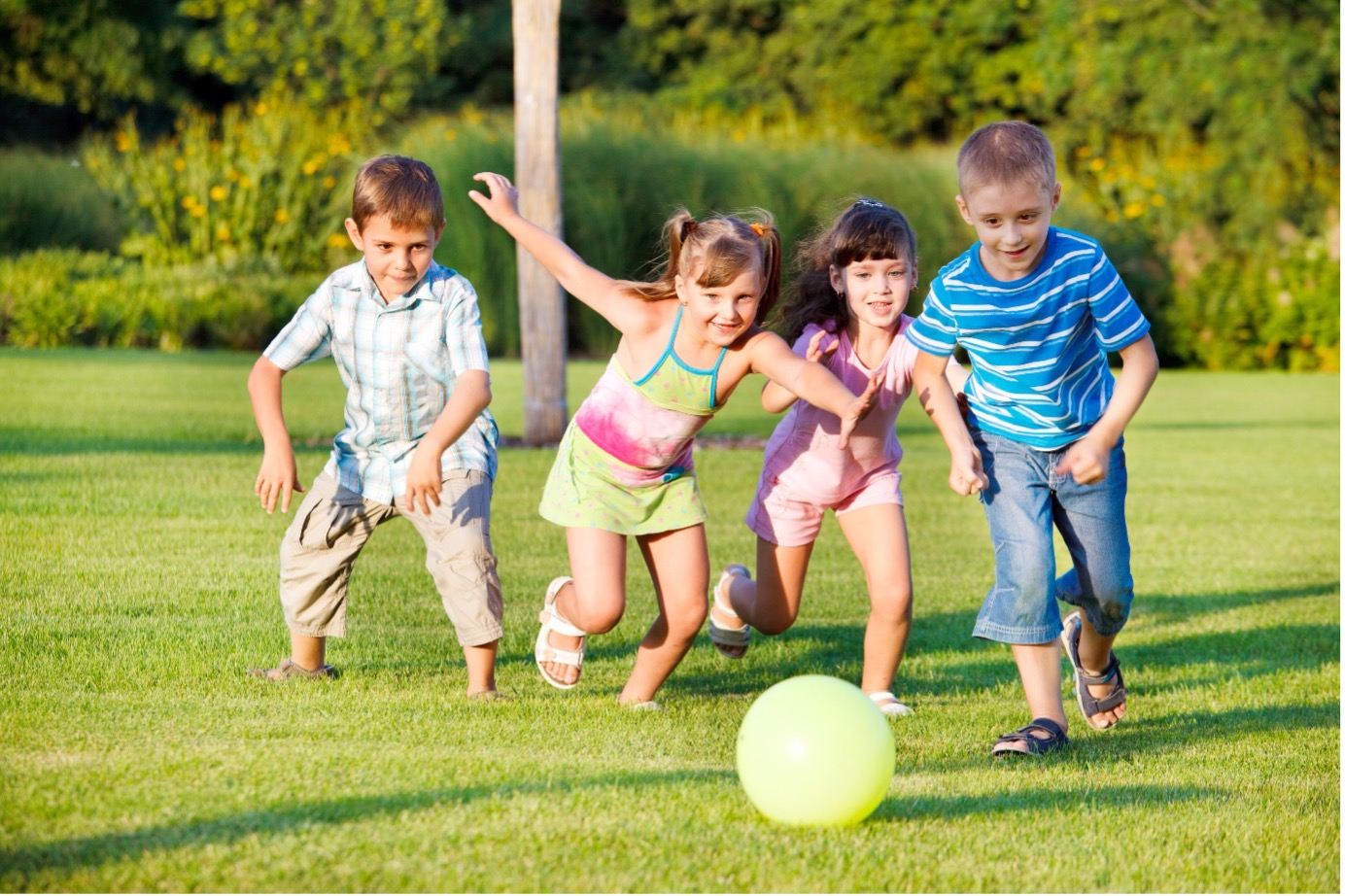 Young children running after a ball outside on the grass.