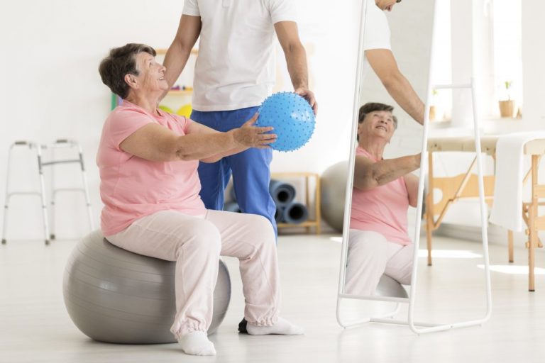 Image of a physiotherapist helping a stroke patient sitting on a therapy ball work on sitting balance and arm function.