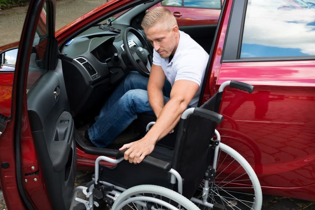 A man with a neurological condition transferring out of a red vehicle into a wheelchair