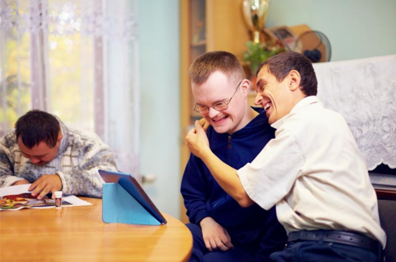 Two smiling people with disability seated at a table and using an iPad 