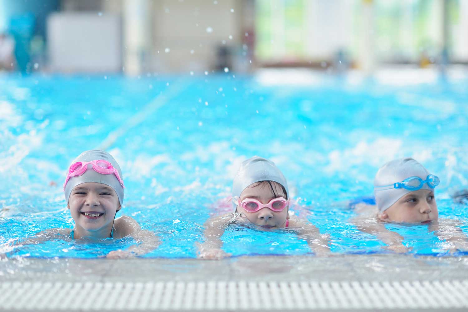 Three children lined up inside the edge of a pool to do their swimming lessons
