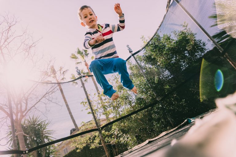 Child with autism doing jumping exercises on a trampoline in the backyard