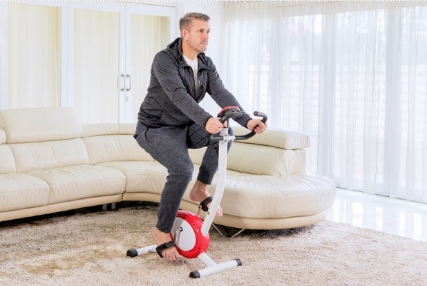 Man using a stationary bike in his loungeroom as part of physiotherapy treatment for Huntington’s disease.