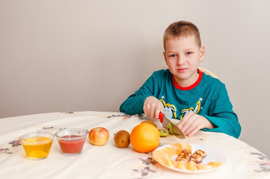 Boy with autism sitting at his kitchen table and cutting up pieces of fruit.