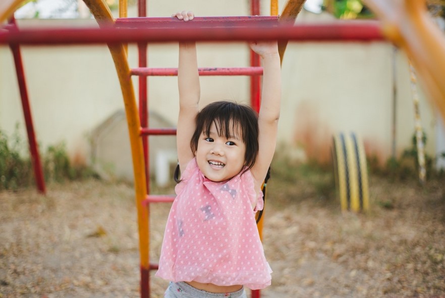 A young girl with autism wearing a pink shirt and swinging on playground equipment.