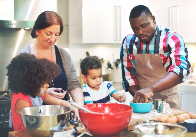 A mother, father, son and daughter cook at a kitchen bench, surrounded by bowls of different colours.